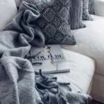 Gray throw blanket draped across a white sofa with patterned pillows