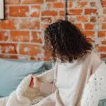 Adult wrapped in an oversized blanket while sitting on a sofa