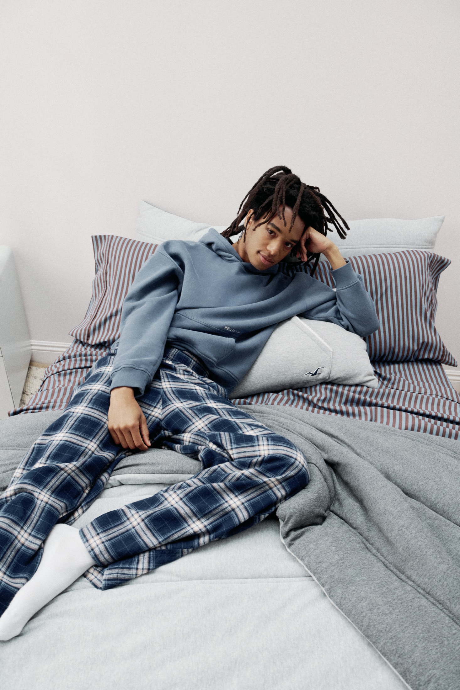Model wearing blue Hollister loungewear on coordinating striped bedding from the Hollister x Target collection