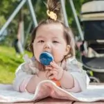 Baby seated on a blanket outdoors with a stroller nearby