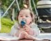 Baby seated on a blanket outdoors with a stroller nearby
