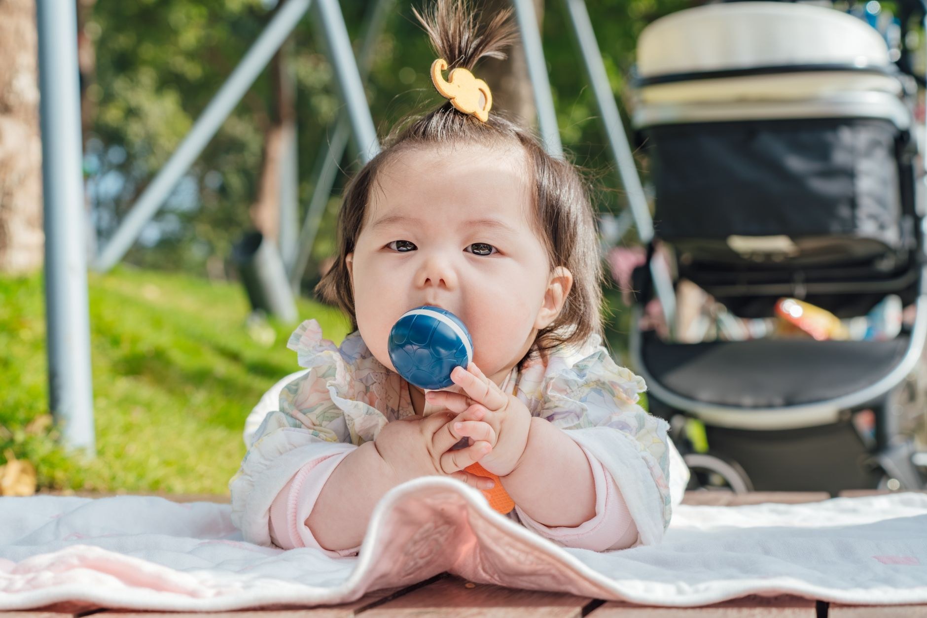 Baby seated on a blanket outdoors with a stroller nearby