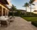 Warm-toned paver patio connecting a covered outdoor seating area with a tropical garden