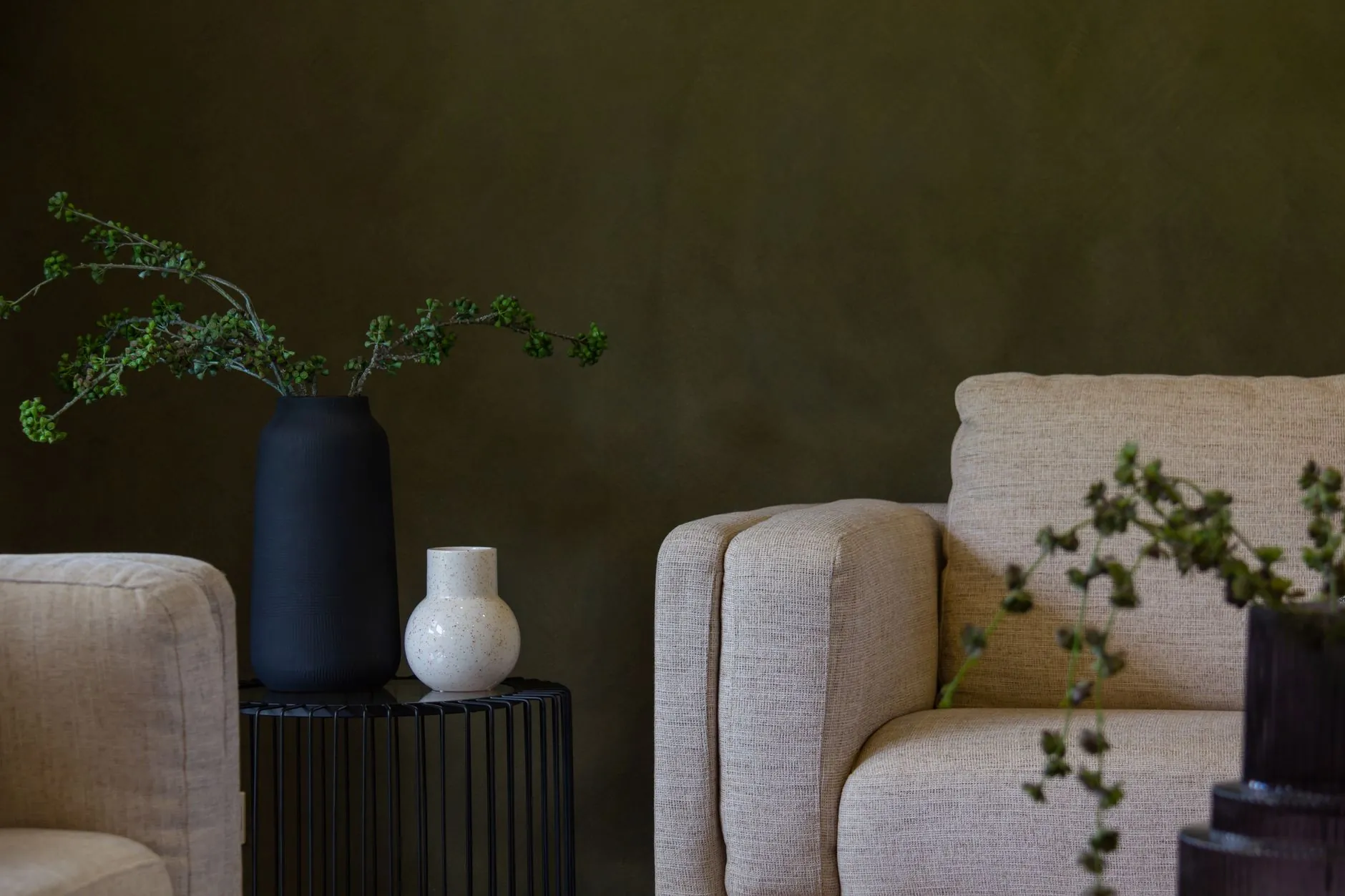 Olive-green wall behind cream armchairs and dark vases in a warm living room