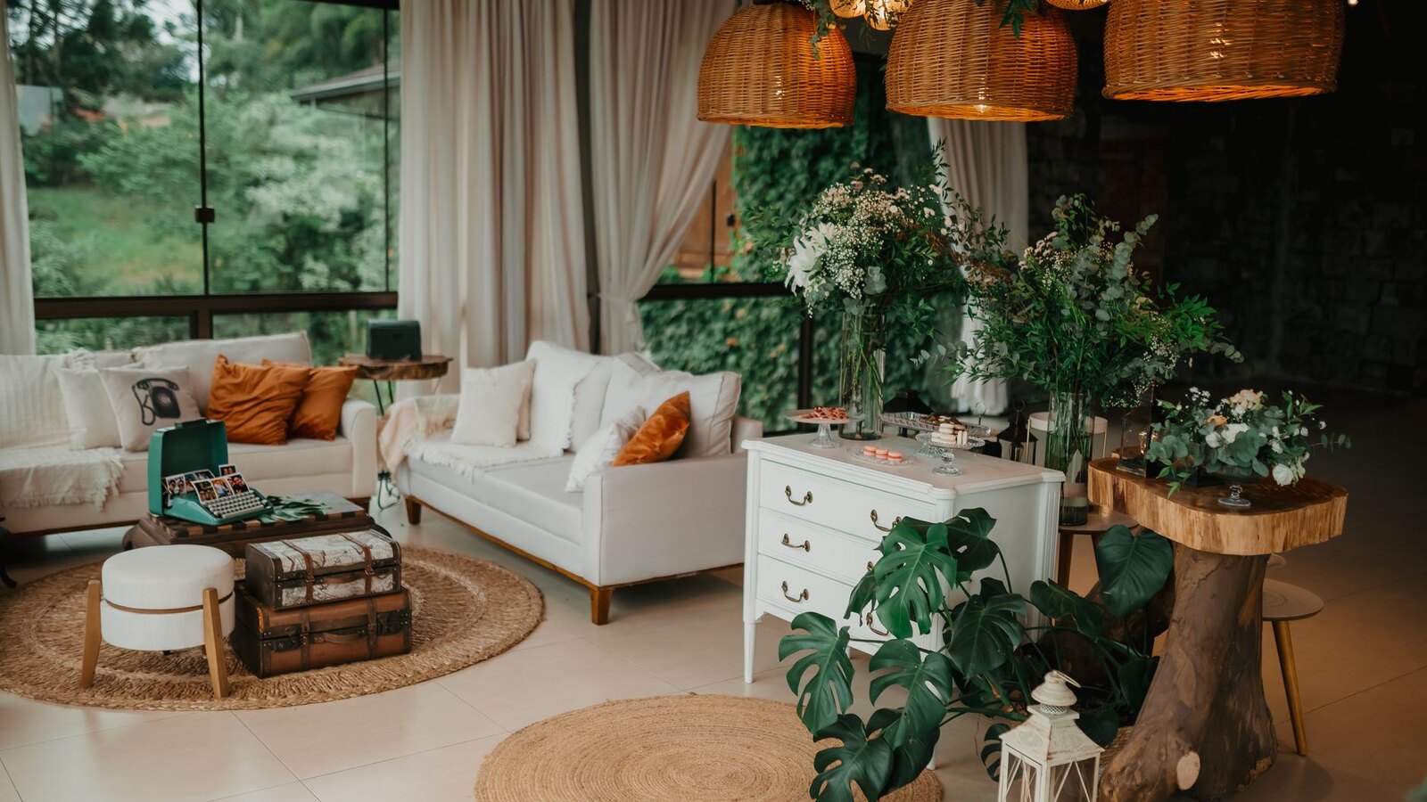 A bohemian living room with rattan pendant lights, jute rugs, white sofas, and layered greenery