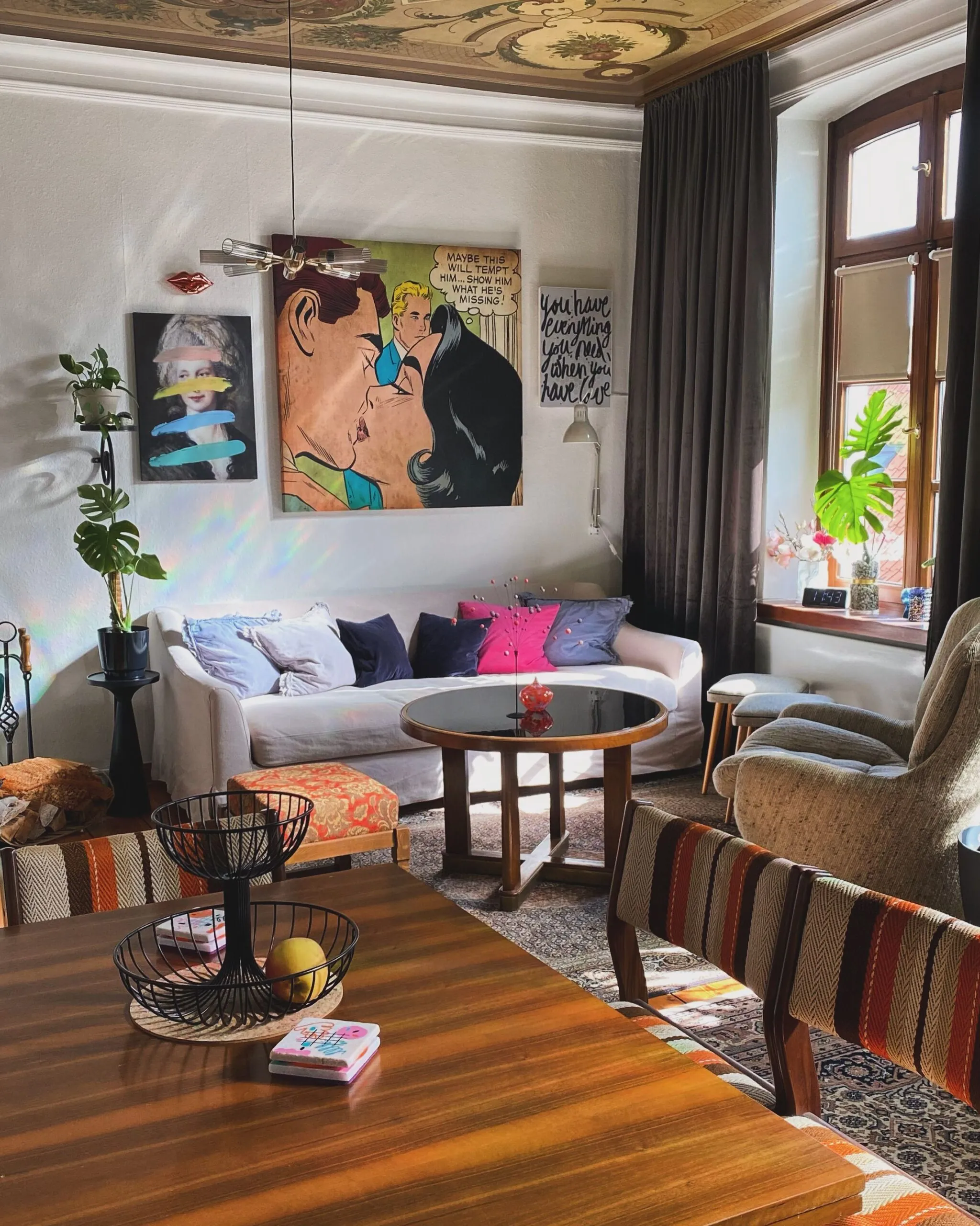 Eclectic living room with layered artwork, vintage furniture, rugs and plants