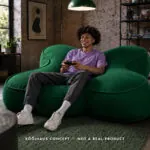 Kooihaus concept illustration: a person gaming on an oversized green D-pad-shaped lounge in a loft. Not a real product.