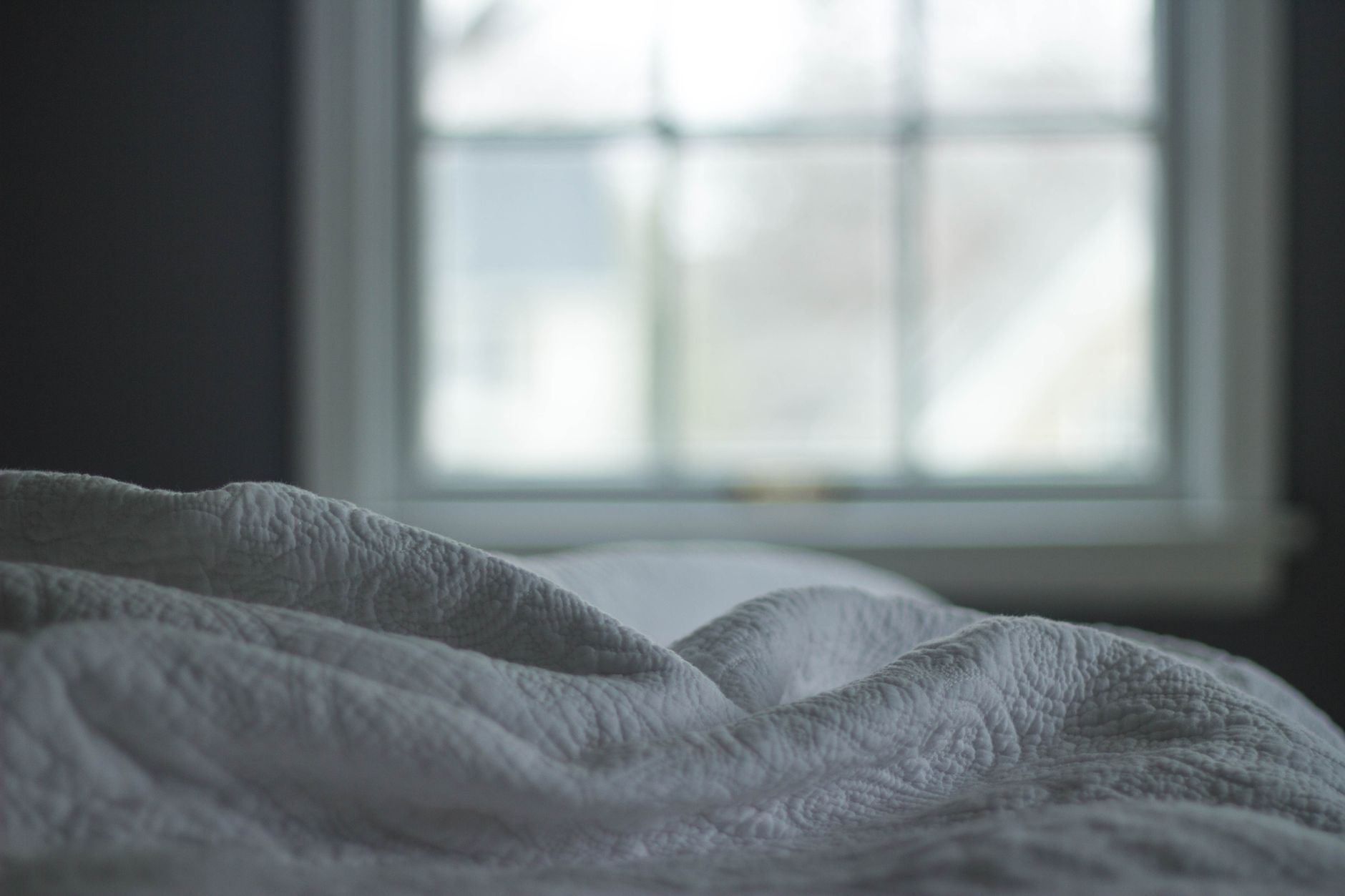 Close view of a quilted white blanket beside a softly lit window
