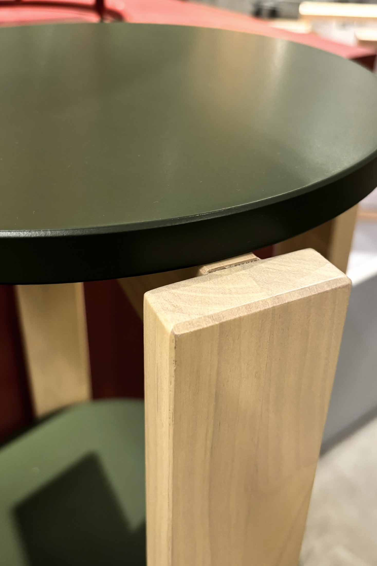 Close view of the painted green edge of an IKEA KOMPISHÄNG stool seat, showing a uniform painted surface with no visible wood grain