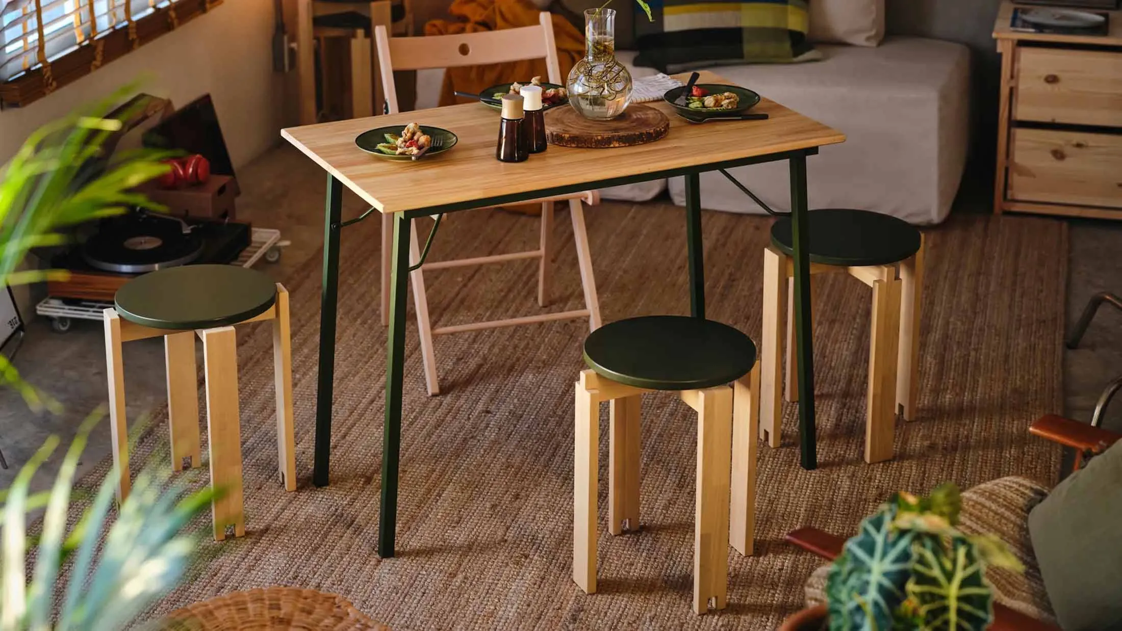 Two IKEA KOMPISHÄNG stools at a dining table in an apartment, with a rug, records and plants around them