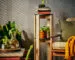 Two IKEA KOMPISHÄNG stools interlocked into a two-tier pedestal, with a potted plant on the lower green seat and books and a glass vessel on the upper one
