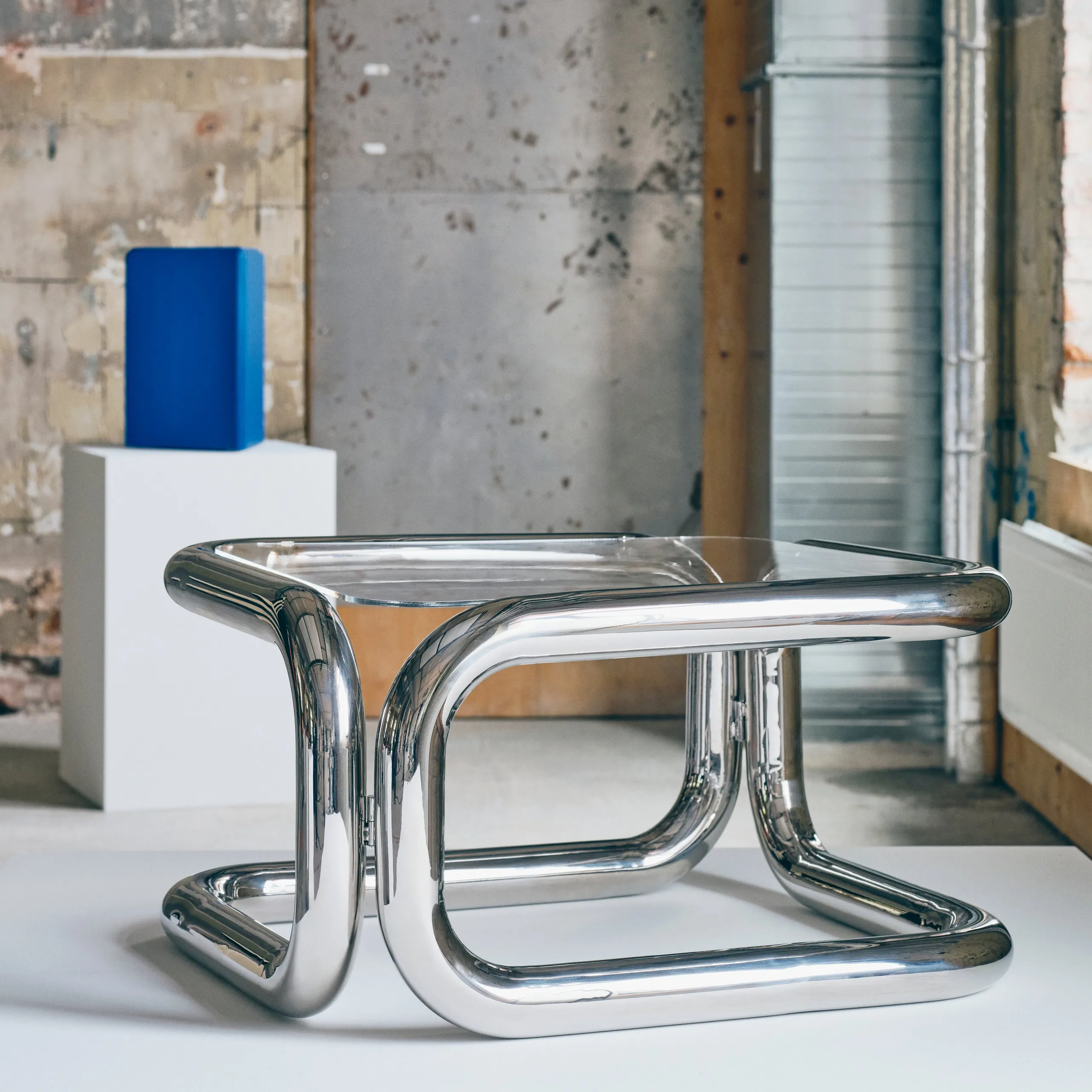 KONSTRUNDA sculptural chrome table with a glass top displayed on a white plinth