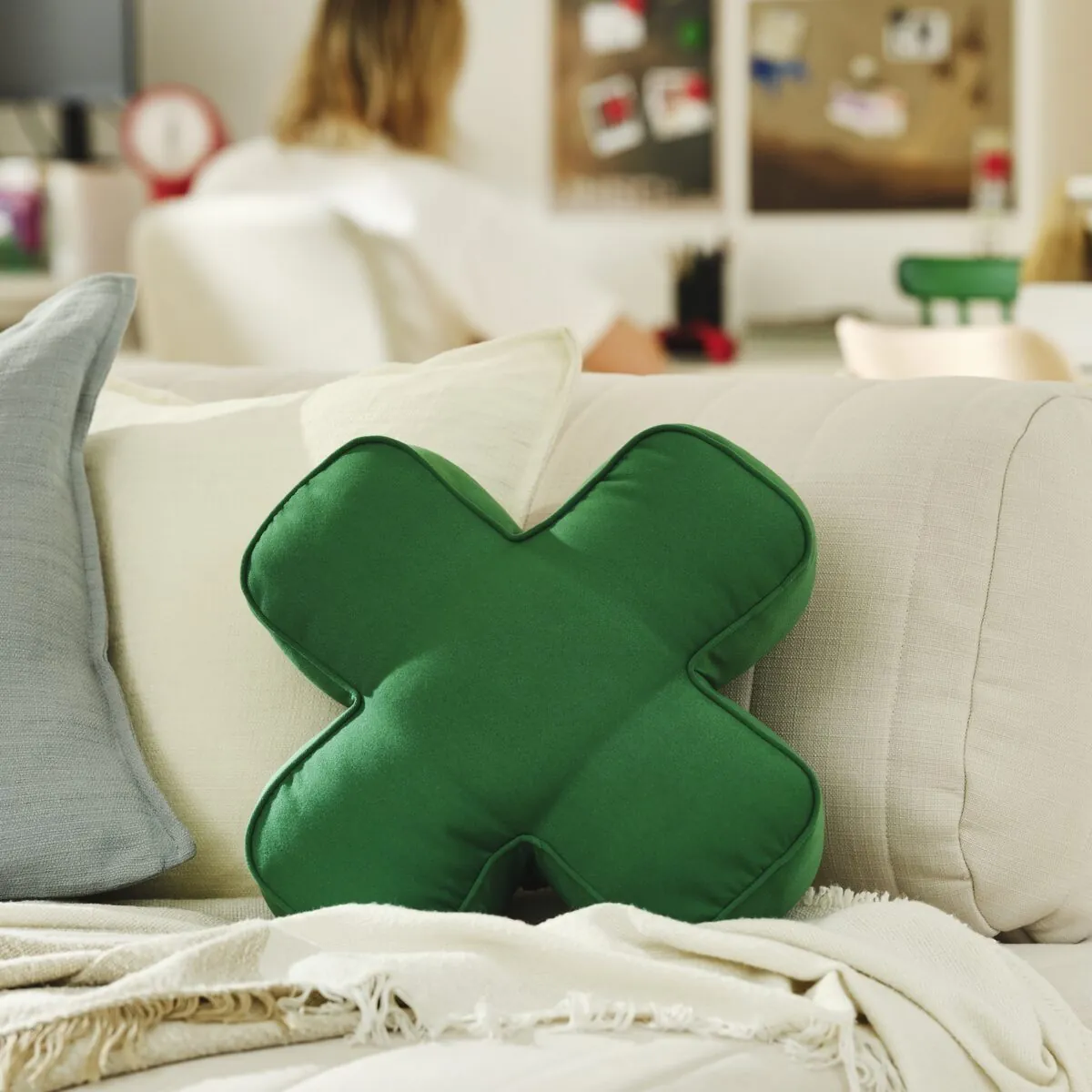 A green cushion inspired by the directional pad of an Xbox controller placed on a sofa