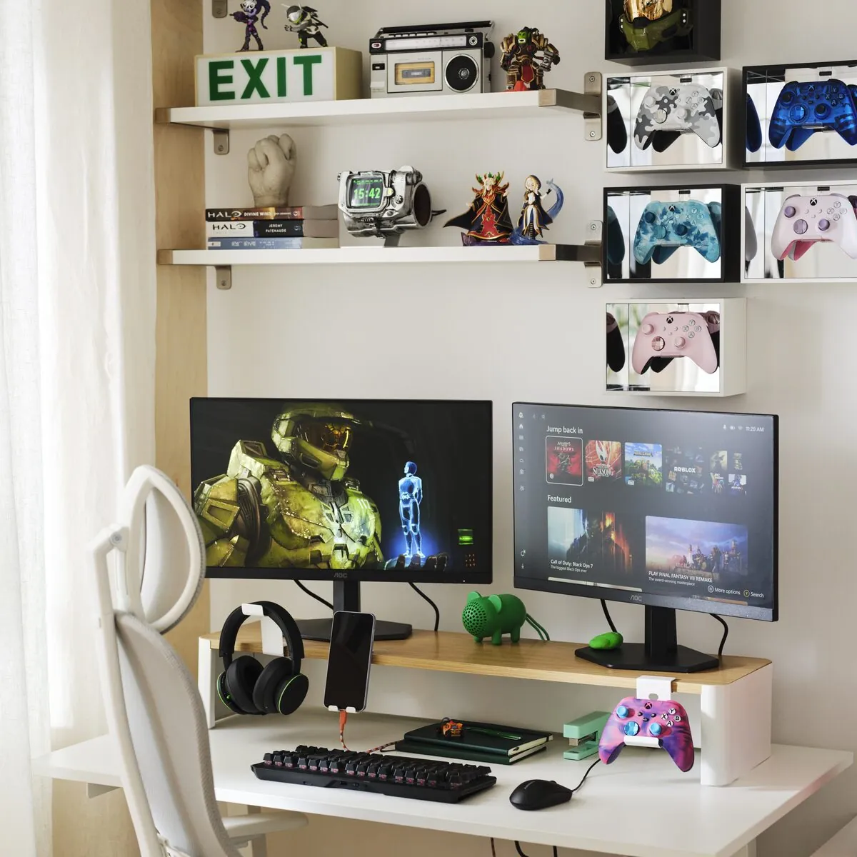 A monitor stand supporting two computer monitors above a desk, with space underneath for headphones, a phone, notebooks and gaming accessories