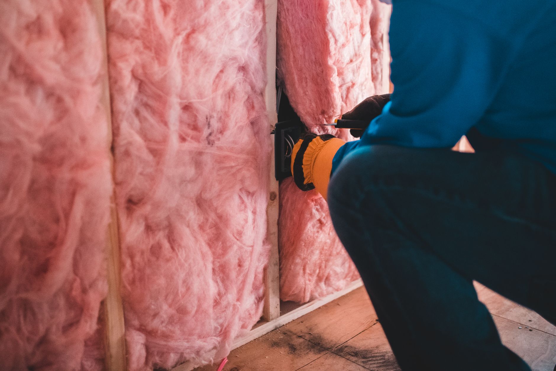 A worker fitting stone wool insulation between wall studs