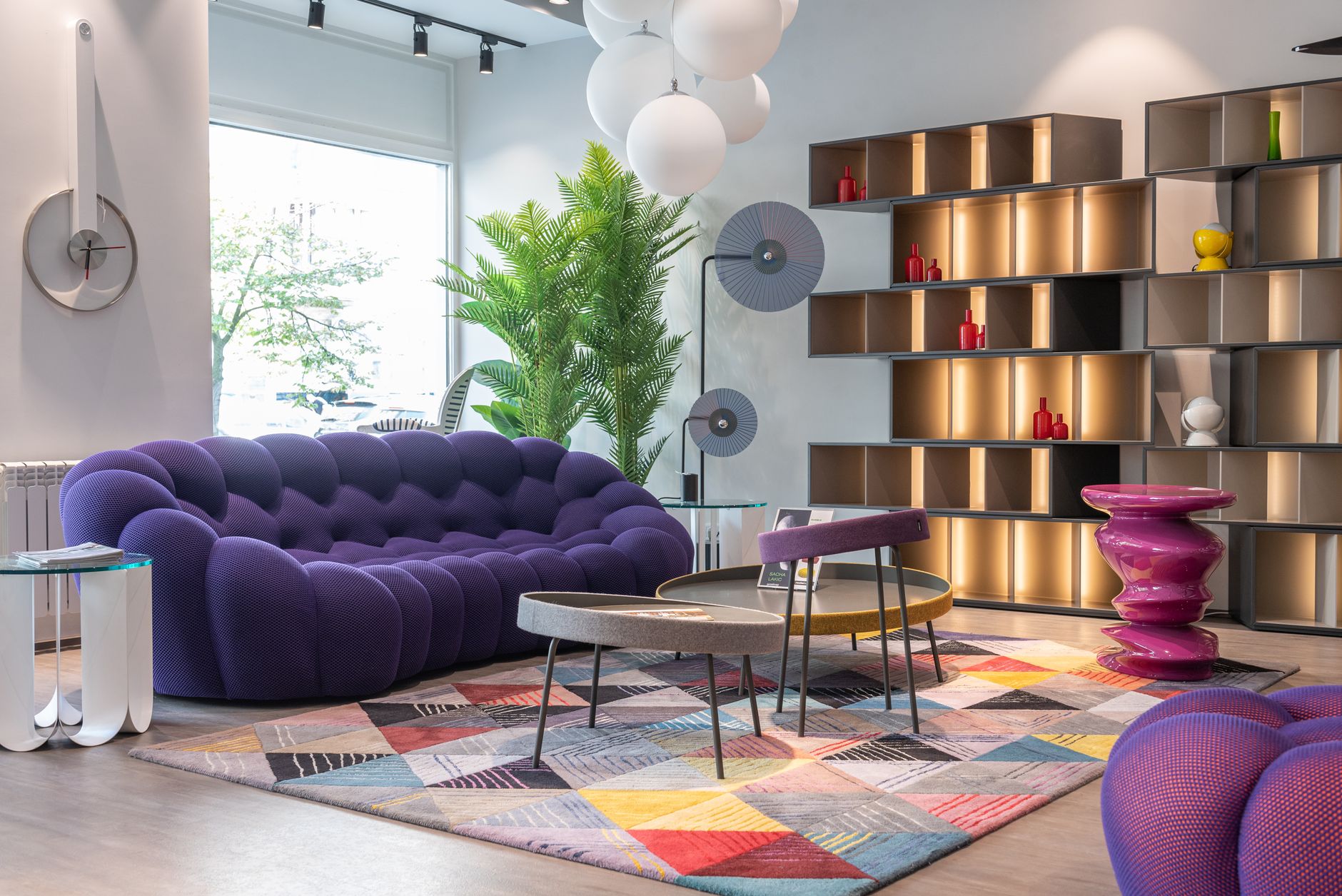 Luxury living room with a sculptural purple sofa, illuminated shelving, and a colorful geometric rug