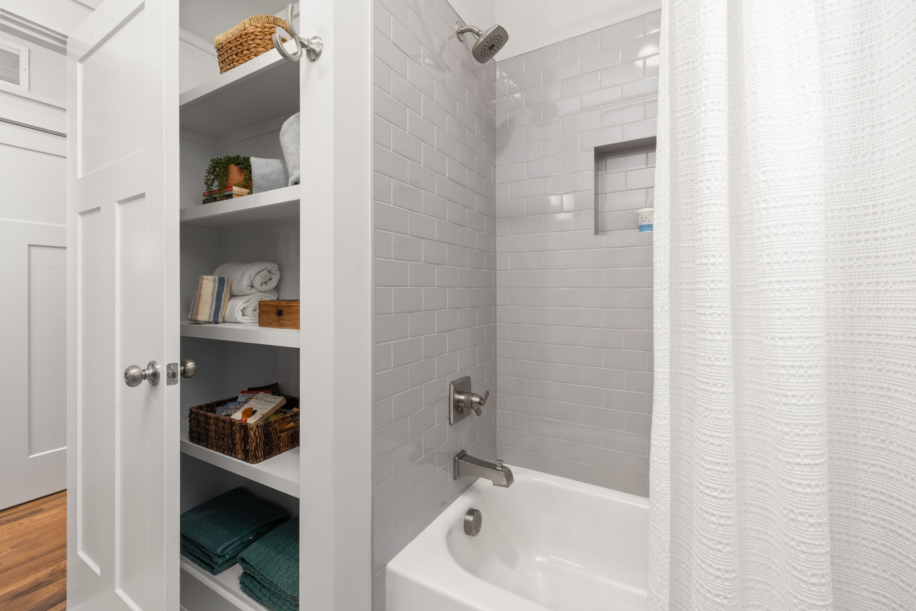 Built-in bathroom shelves holding towels and baskets beside a compact shower