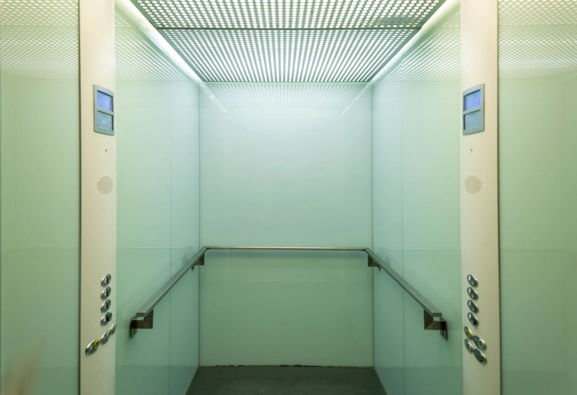 Clean glass-walled elevator cabin with handrails and control panels