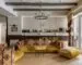 Eclectic living room with a patterned sofa, yellow seating, books, a round table, and mixed lighting