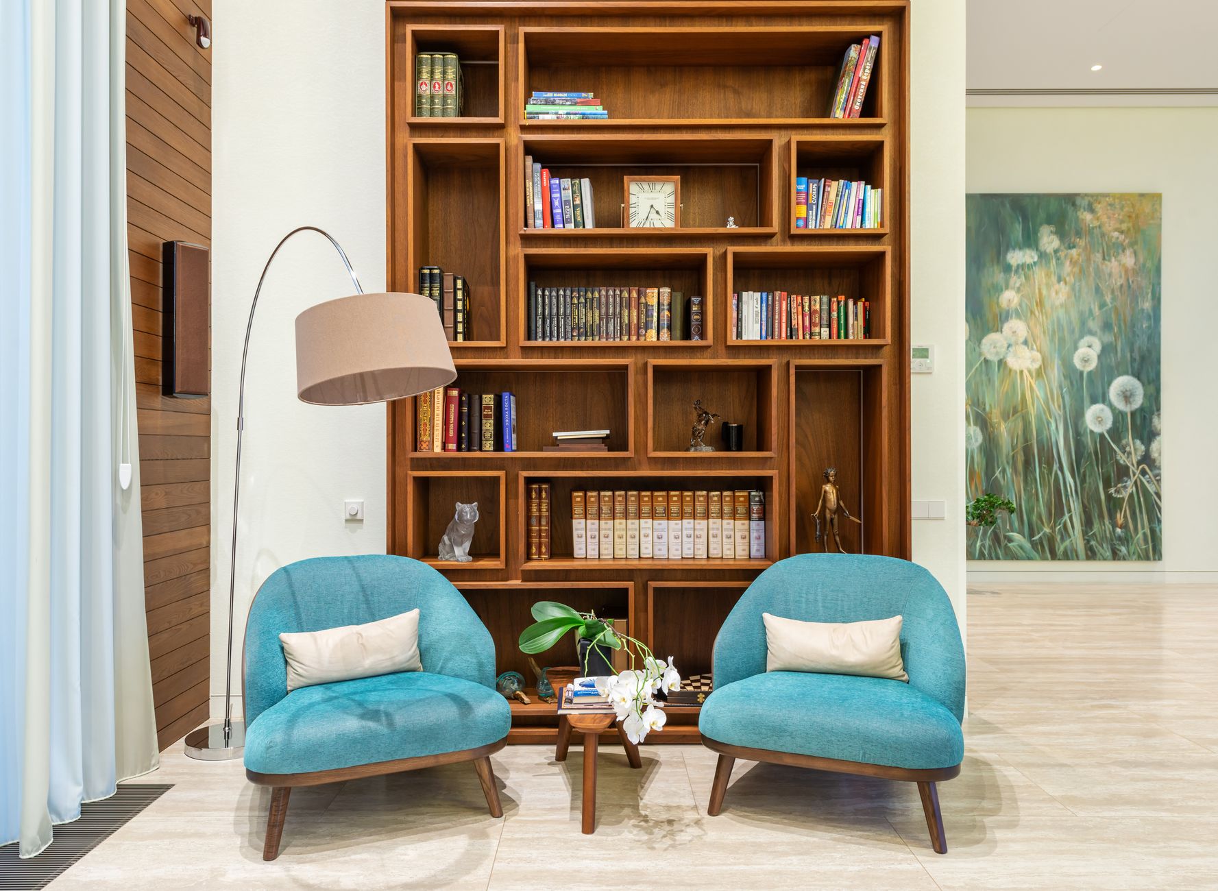 Two blue reading chairs beside a floor lamp and a wall of books