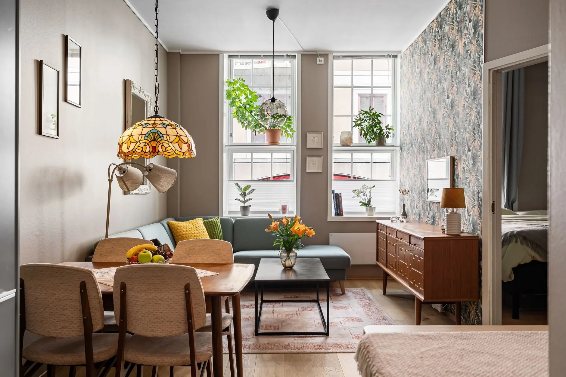 Eclectic living room with a patterned stained-glass pendant, plants, wallpaper, and mixed furniture shapes