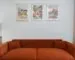 Rust-colored sofa beneath three coordinated framed art prints in a modern living room