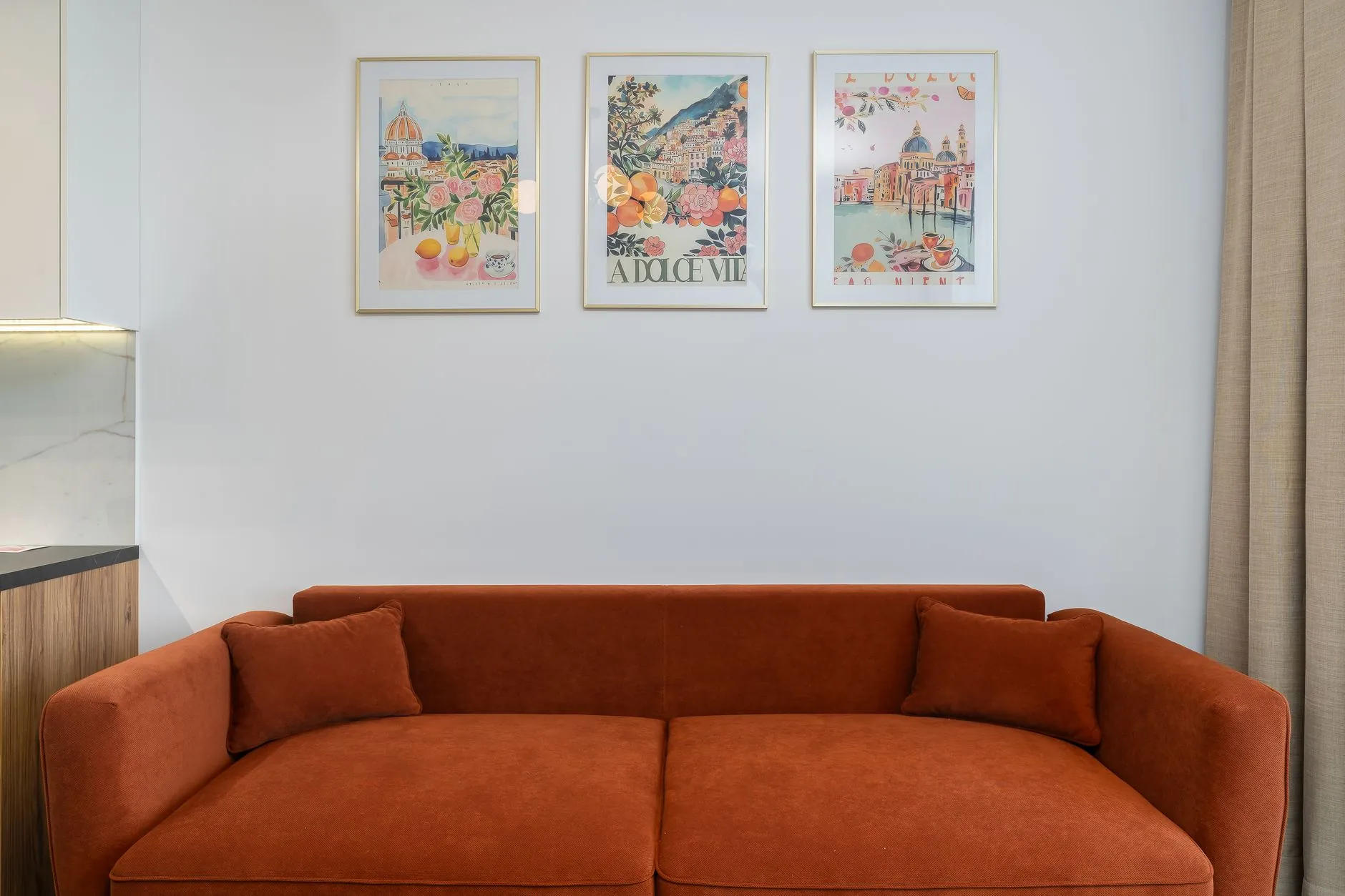 Rust-colored sofa beneath three coordinated framed art prints in a modern living room