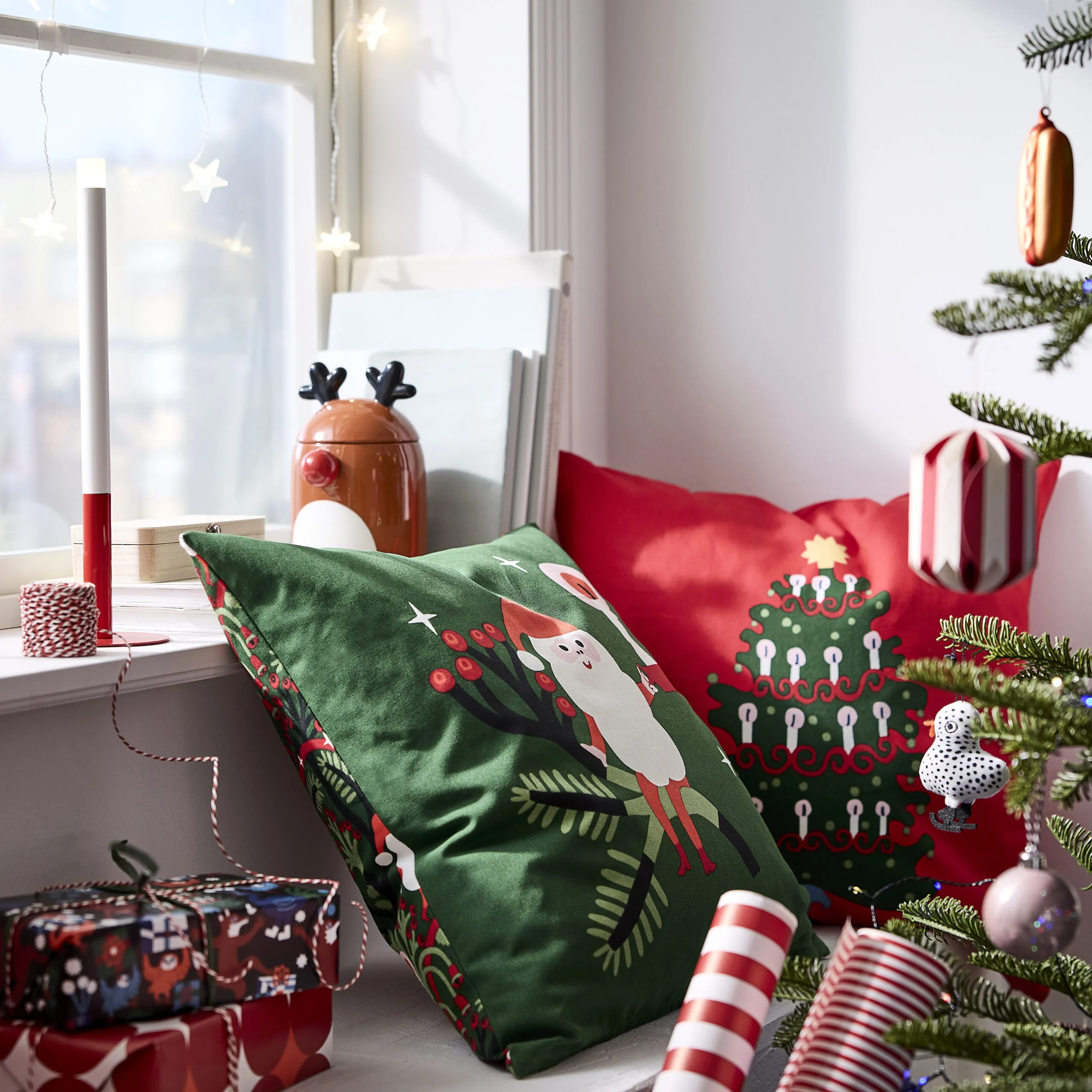 Green and red VINTERFINT Christmas cushion covers styled beside ornaments and gifts