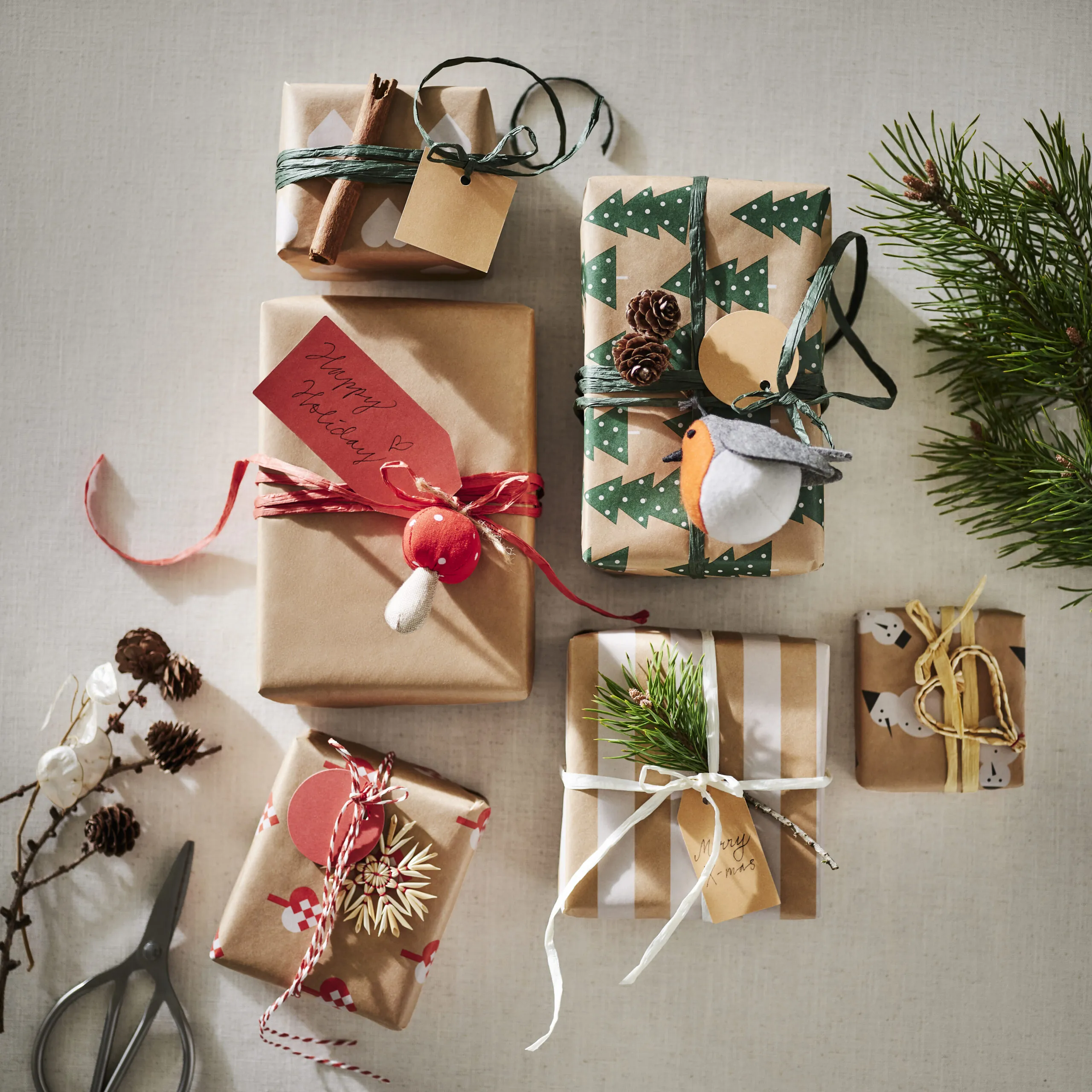 Wrapped gifts with VINTERFINT paper, tags, ribbons, pine cones, and evergreen sprigs