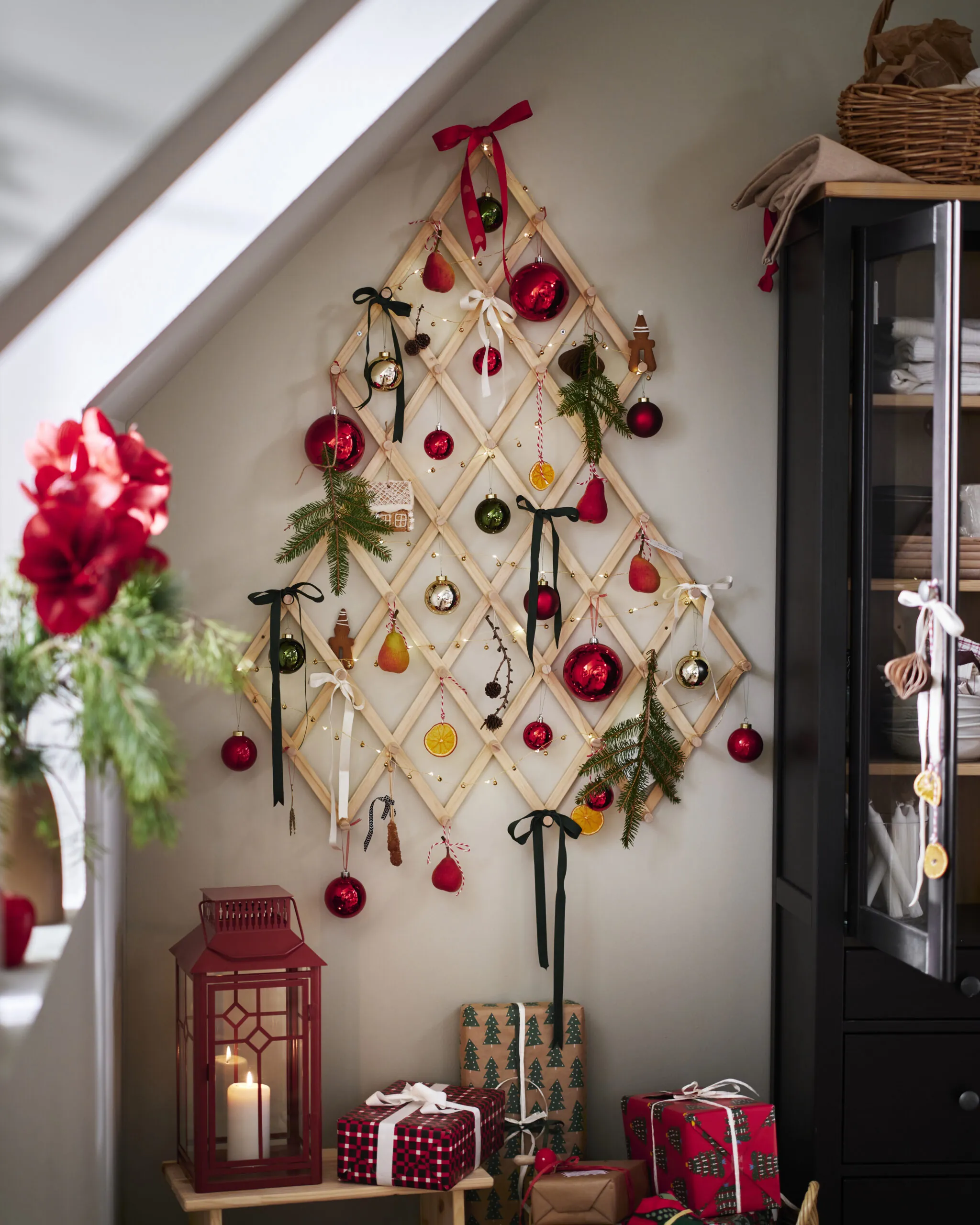 A wall-mounted wooden Christmas tree decorated with ornaments, lights, ribbons, and greenery
