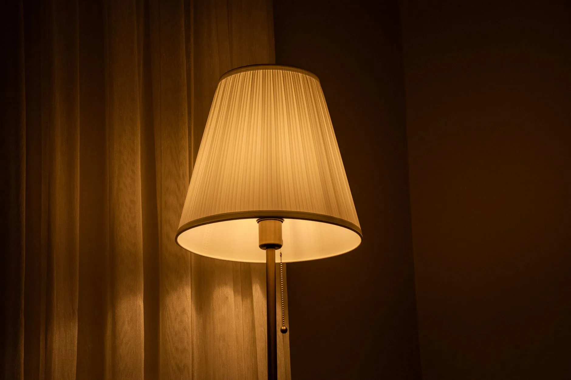 Table lamp casting warm amber light against dark curtains