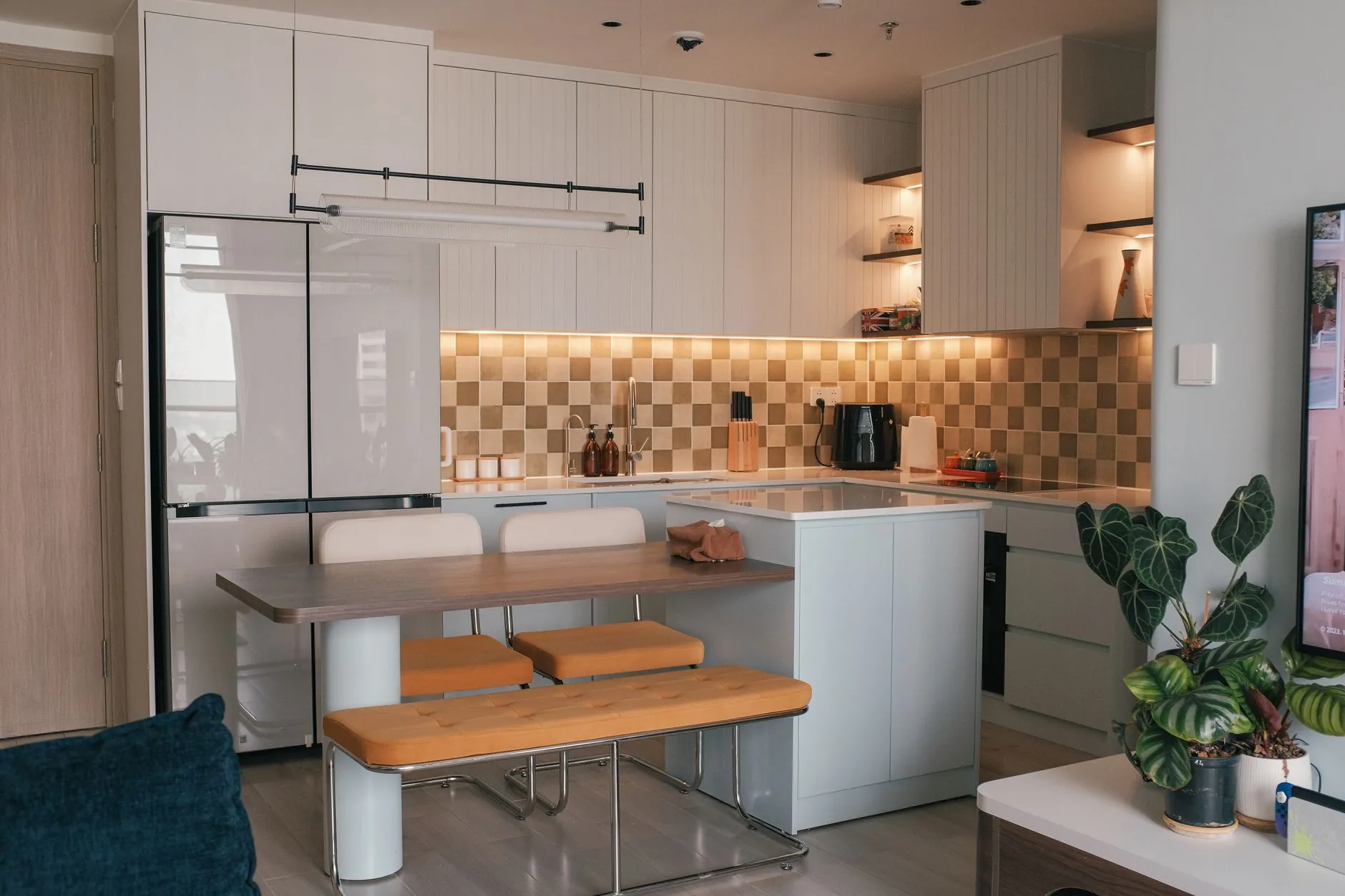 Warm modern kitchen with upholstered bench seating, wood table, plants, and layered lighting