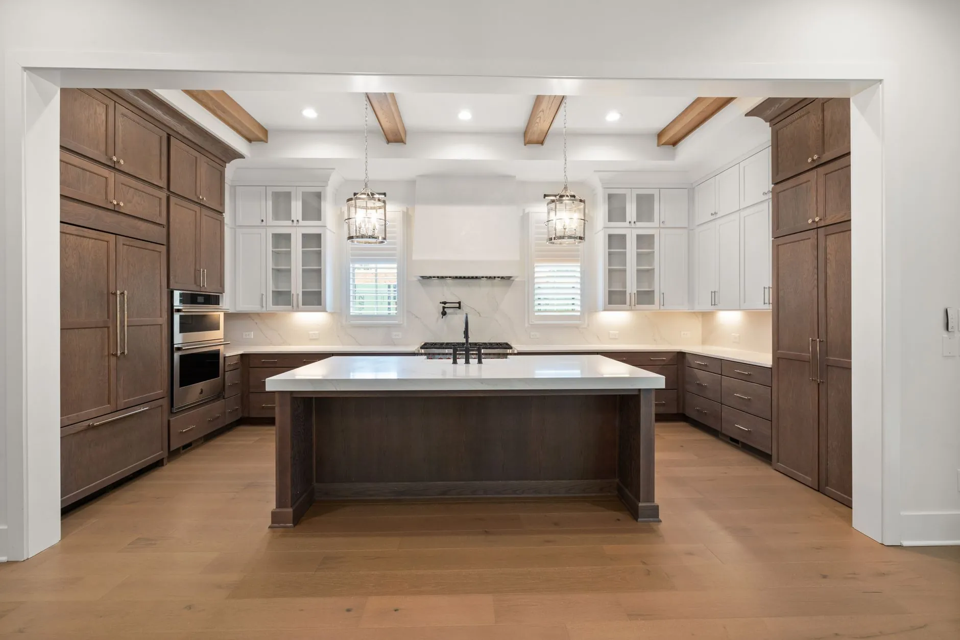Wood and white kitchen with an island, clear work surfaces, and layered pendant and task lighting