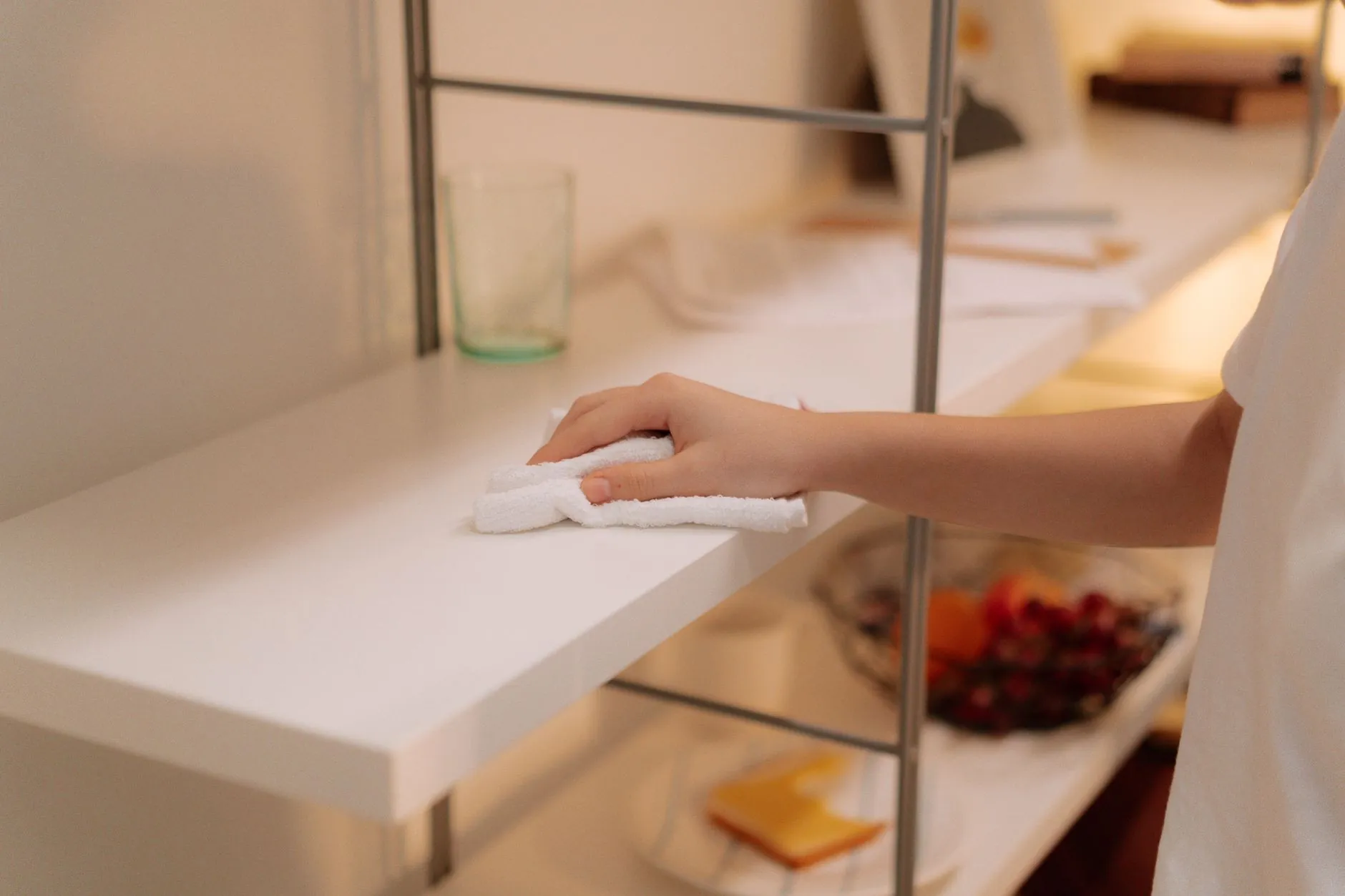 A hand wiping a white shelf with a soft cloth