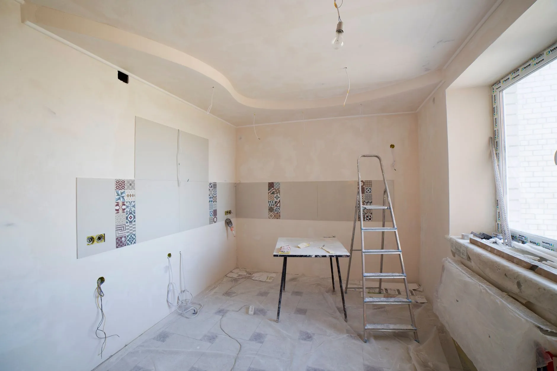 Unfinished kitchen with a ladder, worktable, and exposed service points