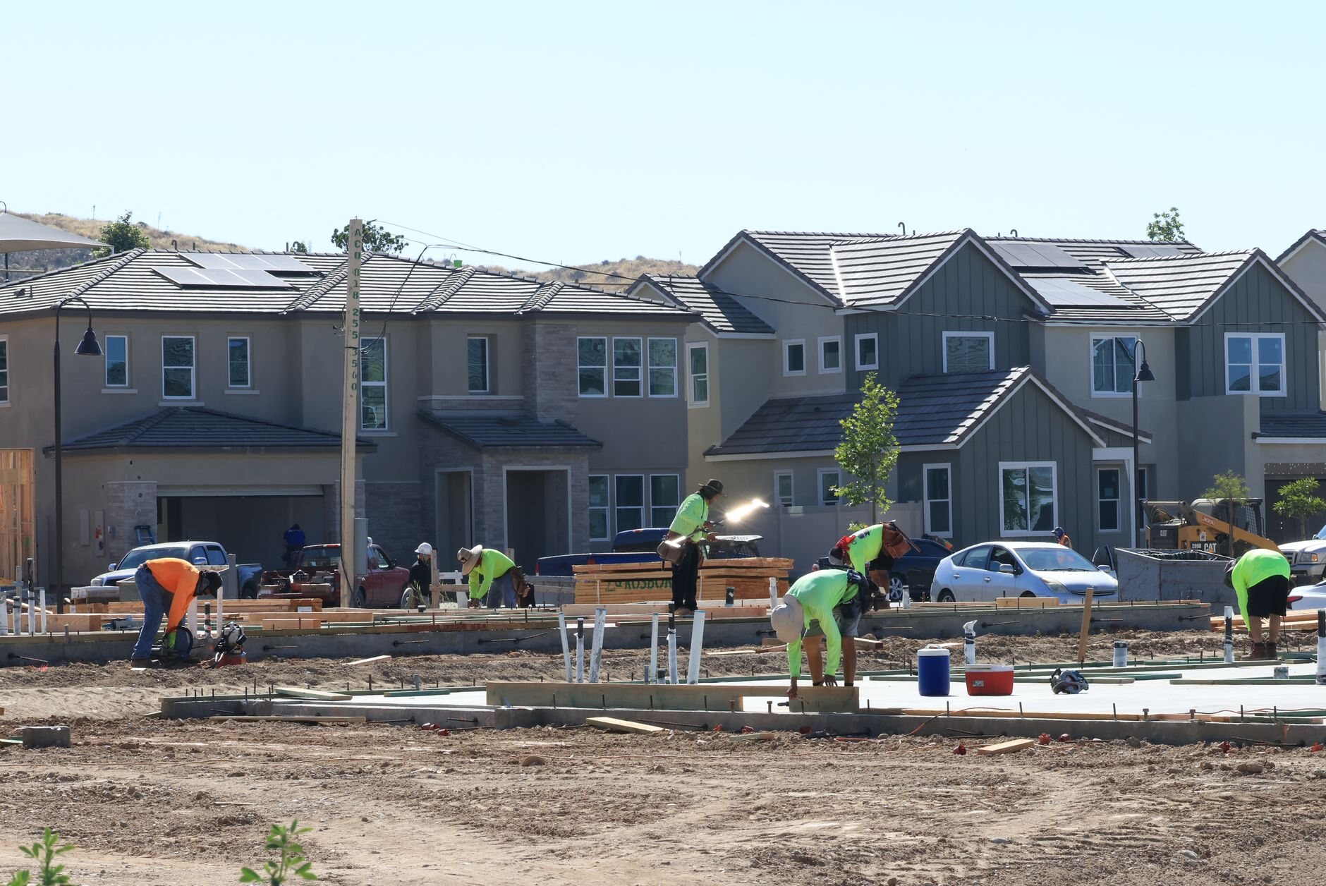 Workers preparing foundation slabs on a new housing development with finished houses behind