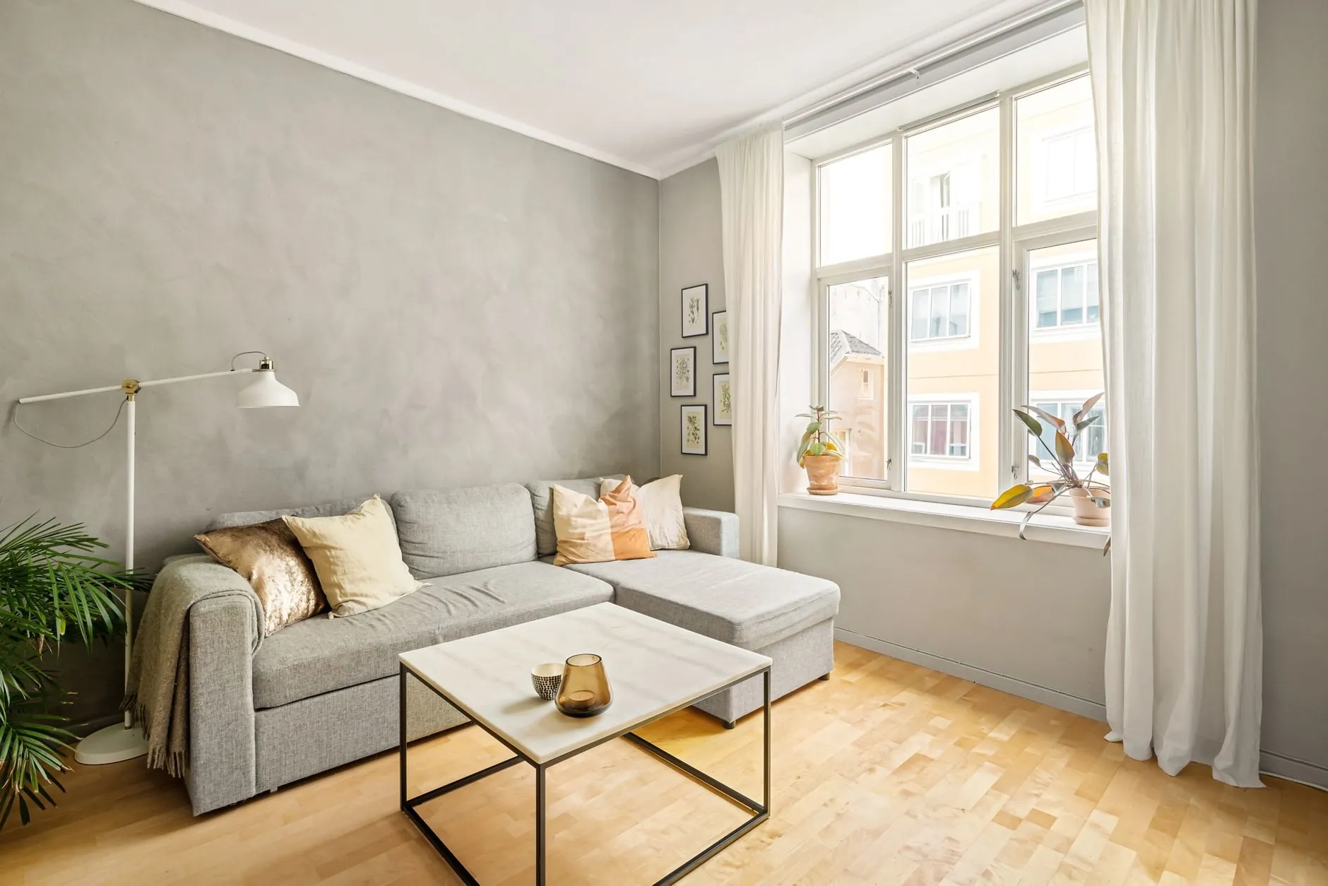 Bright living room with a gray sofa, light wood floor and a large window letting in natural light