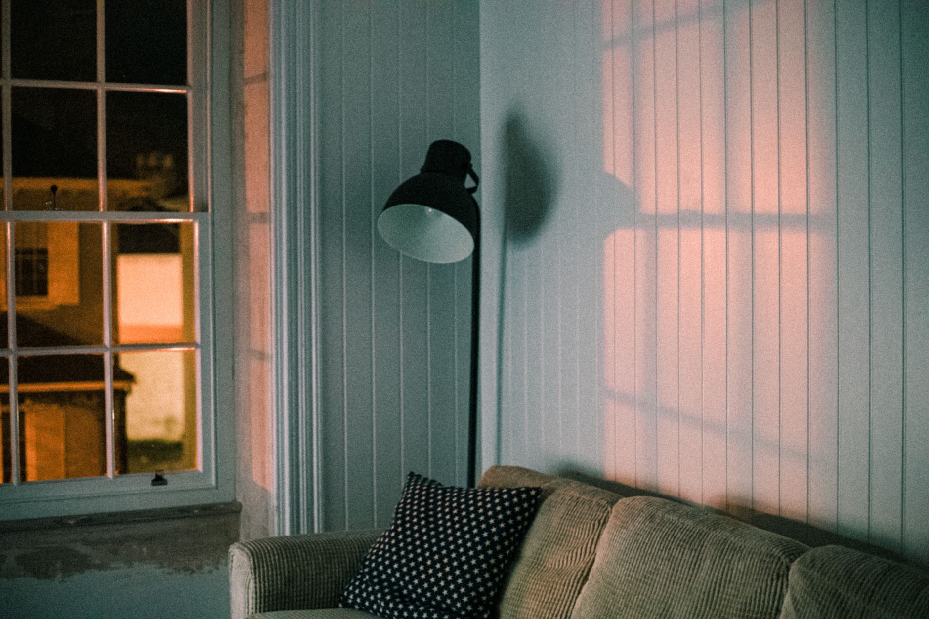 Warm floor lamp casting light and shadows across a living room wall